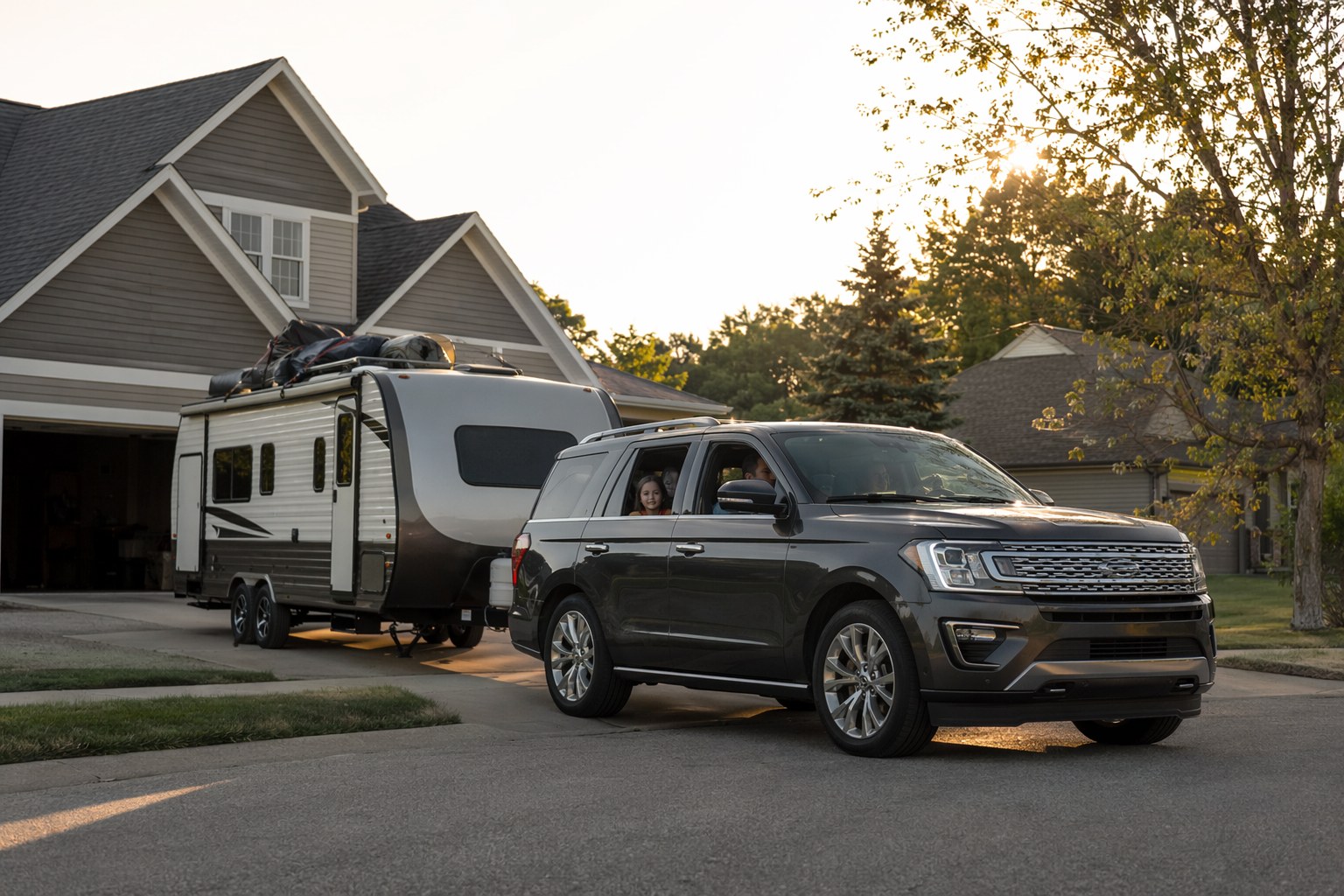 A family pulling out of the driveway for the first camping trip of the season, RV loaded, early morning, kids in the back