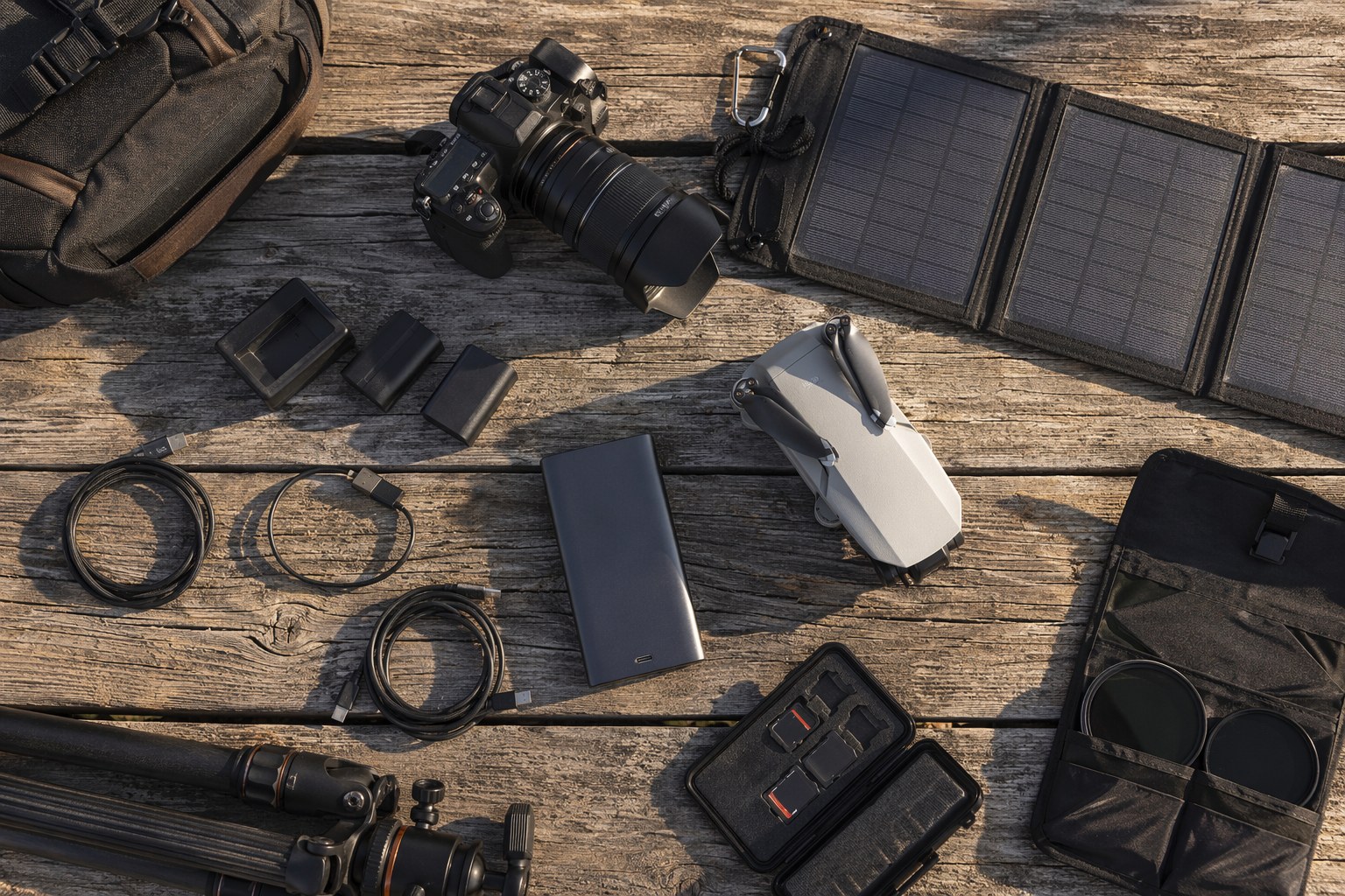 Flat lay of photographer gear including power bank, cables, spare batteries, drone, and folding solar panel